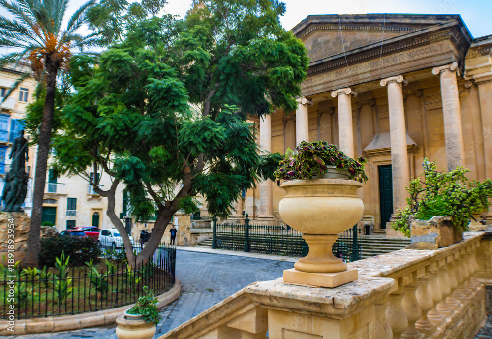 Obraz premium Stone vase with green plants, St Paul s Pro-Cathedral in the background, Independence Square, Valletta, Malta
