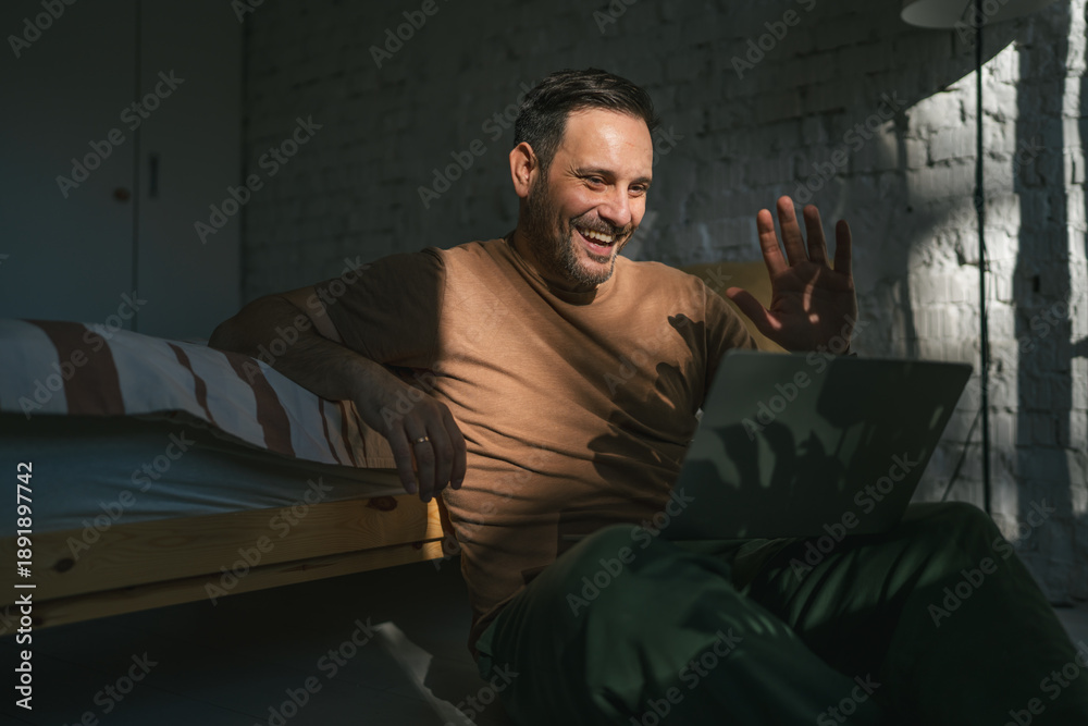 Fototapeta premium Man video calling smiling and waving enjoying remote connection