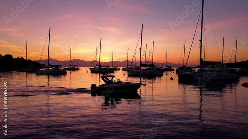 Tranquil harbor view at sunset with silhouettes of sailboats and a motorboat, reflecting on calm water