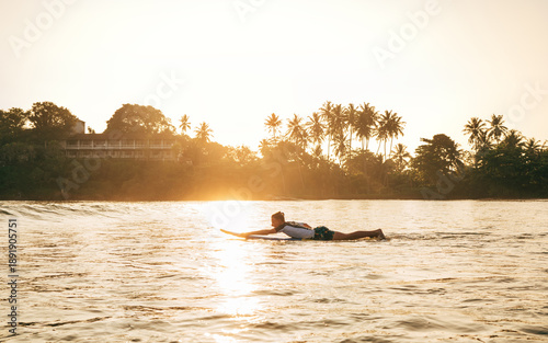 Photography Young teenager boy paddling on surfboard into sea for surf ride