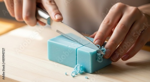 Close-up of person slicing a handmade blue bar of soap on a wooden cutting board, creating small shavings