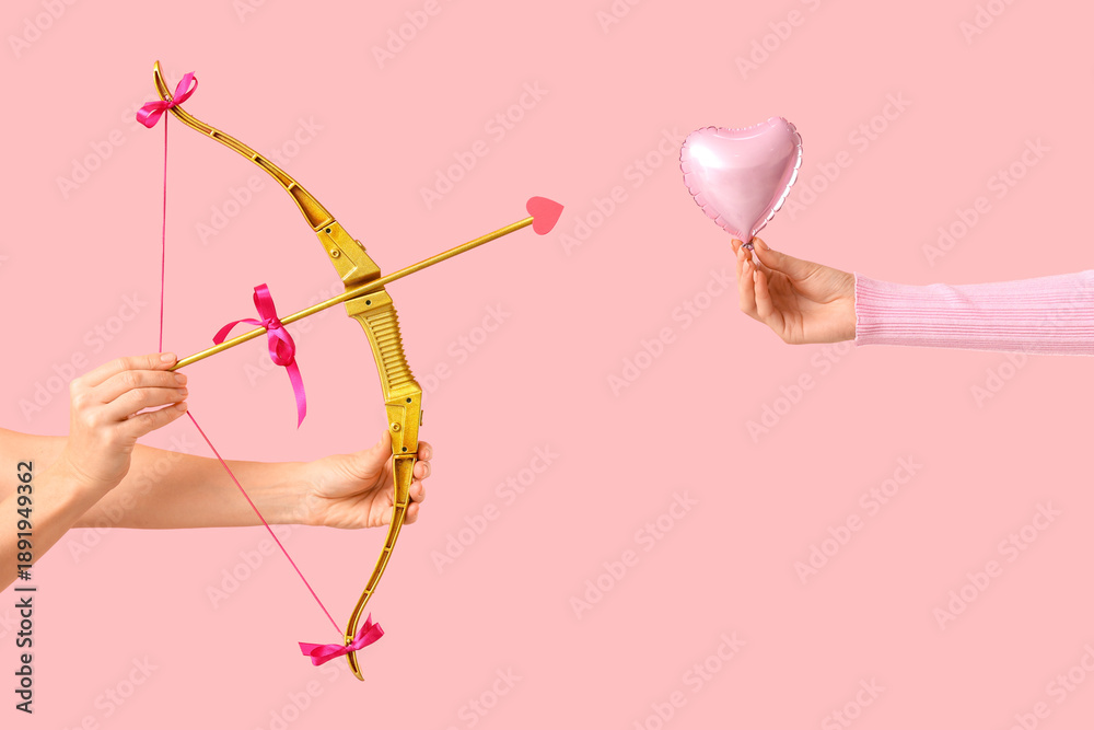 Fototapeta premium Female hands with cupid's bow and heart shaped balloon on pink background. Valentine's Day celebration
