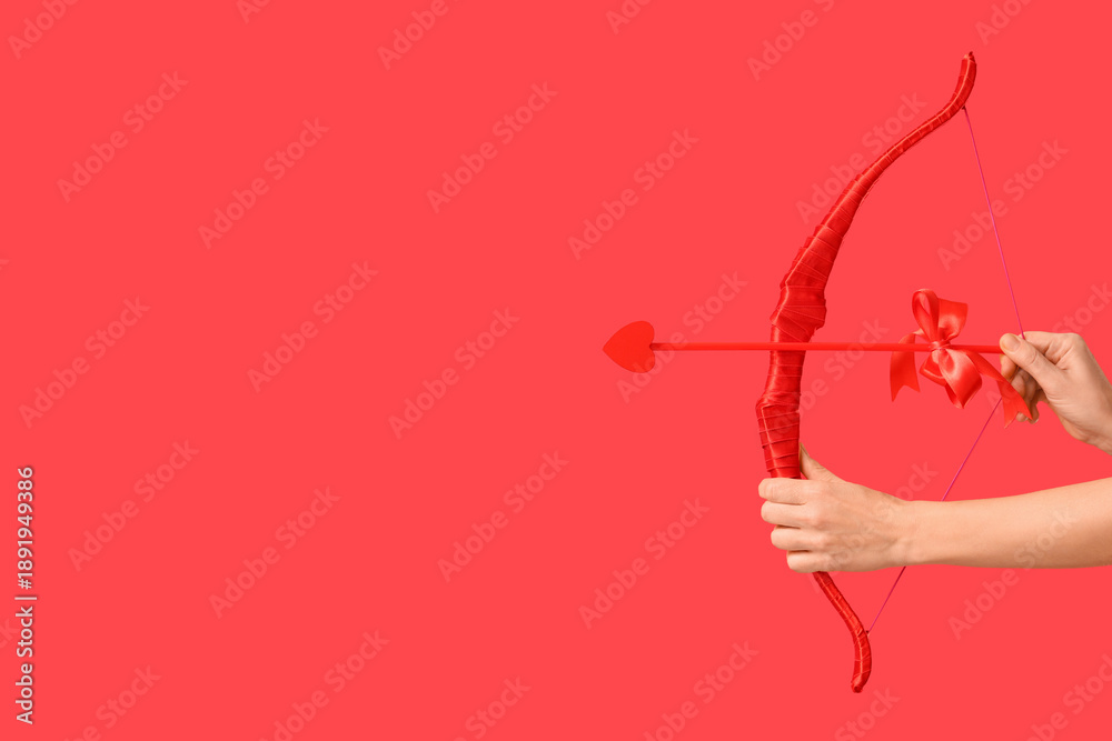 Fototapeta premium Female hands with cupid's bow on red background. Valentine's Day celebration