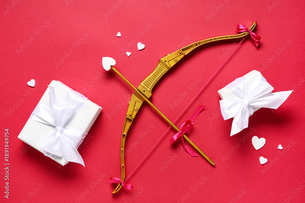 Obraz premium Composition with cupid's bow, gift boxes and paper hearts on red background. Valentine's Day celebration