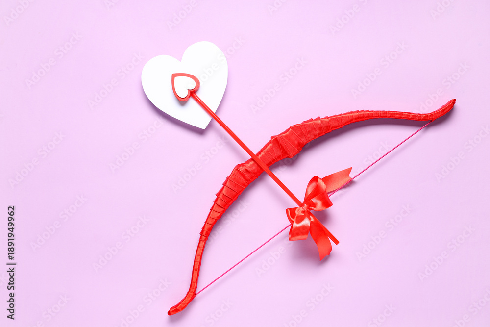 Fototapeta premium Red cupid's bow with paper heart on lilac background. Valentine's Day celebration