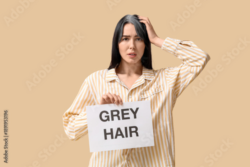 фотографія Young woman holding paper with text GREY HAIR on beige background