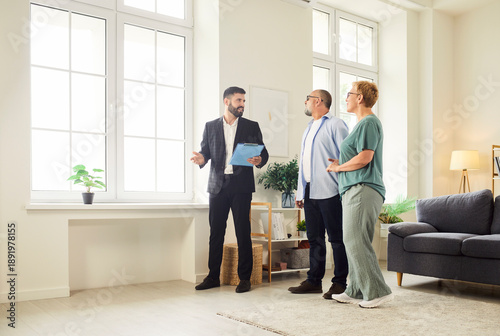 Realtor and agent guide a senior couple through new apartment during a tour and viewing, helping buyers assess the interior and showing key home features. Real estate market and buying property.