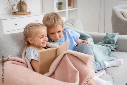 Little kids with plaid reading book on sofa at home
