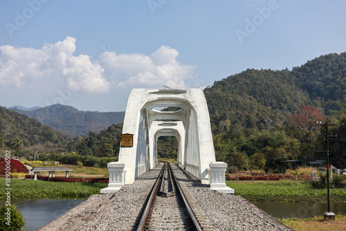 Scenic white railway bridge, beautiful travel destination in Thailand. This architecture provides peaceful view of green mountain landscape on clear day