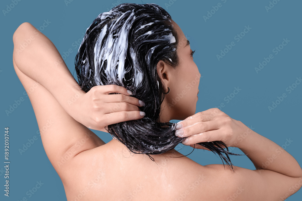 Obraz premium Asian woman applying hair mask on blue background, back view