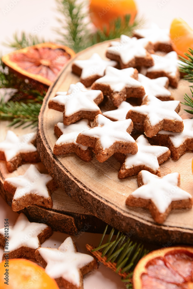 Fototapeta premium Wooden board of star-shaped gingerbread cookies with mandarin, dried orange and fir branches on beige background