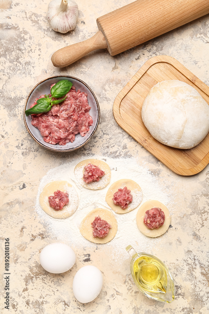Fototapeta premium Raw dough with minced meat and ingredients for preparing dumplings on beige background