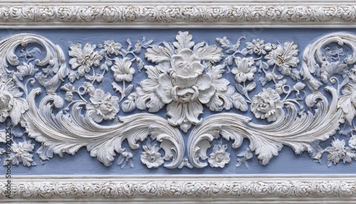 Ornate, intricately carved architectural molding features floral reliefs against a pale blue background.