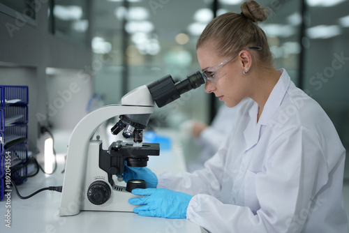 Billede på lærred Side view of Caucasian female scientist looking through microscope in modern lab