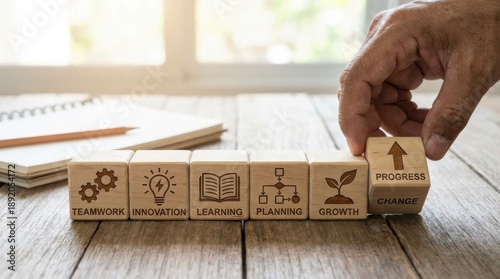 Arranging six natural wooden cubes illustrating business concepts like teamwork, innovation, learning, planning, growth, and progress on a rustic desk.