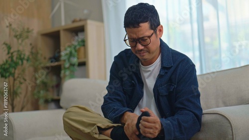 Tableau sur toile Asian Man Massaging His Painful Foot While Sitting on Sofa at Home