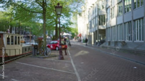 Wallpaper Mural Blurry european city street with defocused background featuring parked cars, bicycles, trees, and buildings, creating a serene urban atmosphere under clear blue sky. Torontodigital.ca