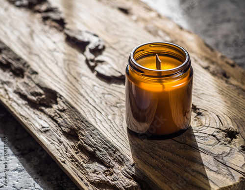 Artisanal Candle Jar Mockup on Rough Wood. Craft & Handmade Authentic Product Display. An unbranded amber glass jar candle with a wooden wick placed on a weathered light oak reclaimed wood plank.
