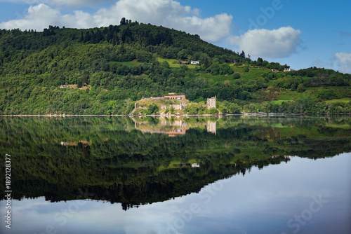 2023-06-12 A OLD CASTLE AND A GREEN HILLSIDE FROM LOCH NESS WITH A BEAUTIFUL REFLECTION IN THE LOCH OUTSIDE OF INVERNESS SCOTLAND