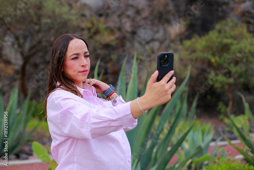 Pregnant woman uses her cell phone to take a selfie outdoors