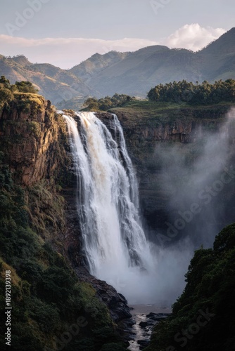 Powerful waterfall cascading down rocky cliffs into a lush green valley for nature tourism and environmental conservation promotion in a majestic mountain landscape