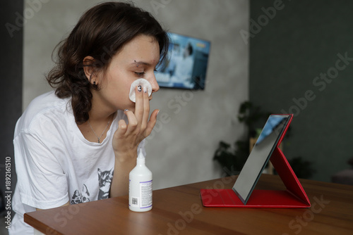 Natural portrait of teenage girl with acne and problematic facial skin at home. A teenager without makeup wipes her forehead with a cotton pad, demonstrating daily skin care for acne. The concept of
