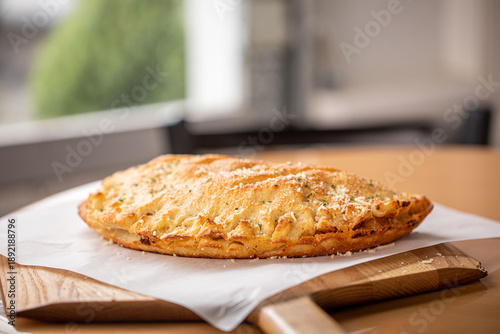 Foto A cheese calzone served on a wooden board at a brightly lit restaurant with gree