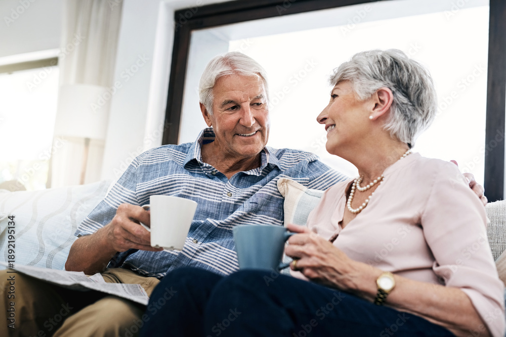 Fototapeta premium Talking, coffee and senior couple on sofa in home for bonding, love and reading together. Newspaper, relax and elderly people in retirement with warm beverage for conversation in living room.