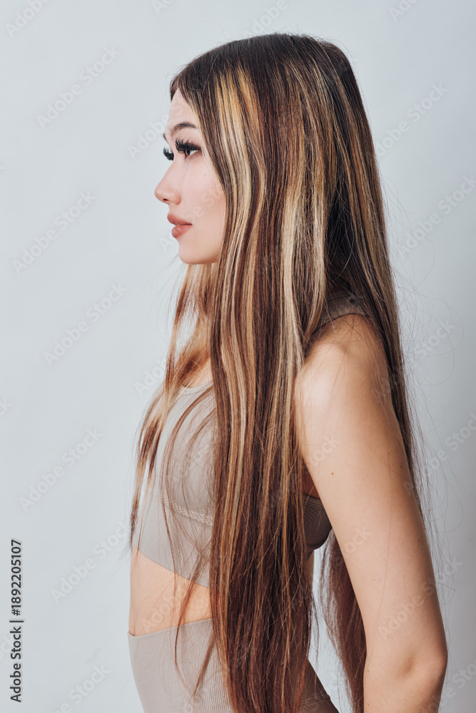 Naklejka premium Young woman with long straight hair and natural makeup in neutral outfit posing in profile on plain background. Beauty, fashion, and casual style concept with serene expression.