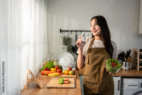 Asian woman eatting healthy salad and drink water in kitchen at home.