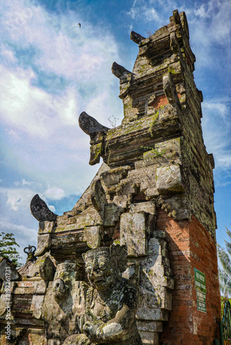 A rustic old Balinese traditional stone statue sculpture in front of the orange brick gate with stone sculpture decoration in Bali, Indonesia