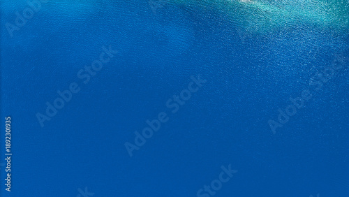 Top view aerial shot of deep blue freshwater reservoir surface with gentle ripples and sunlight reflections.