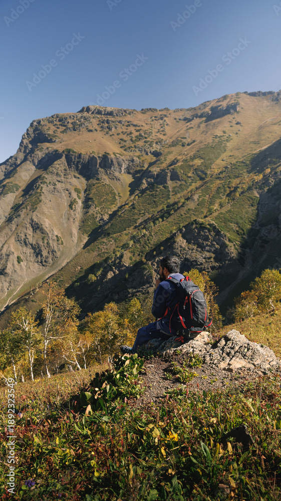 Fototapeta premium Solo Trekker Resting on Rocky Peak Enjoying Scenic Himalayan View