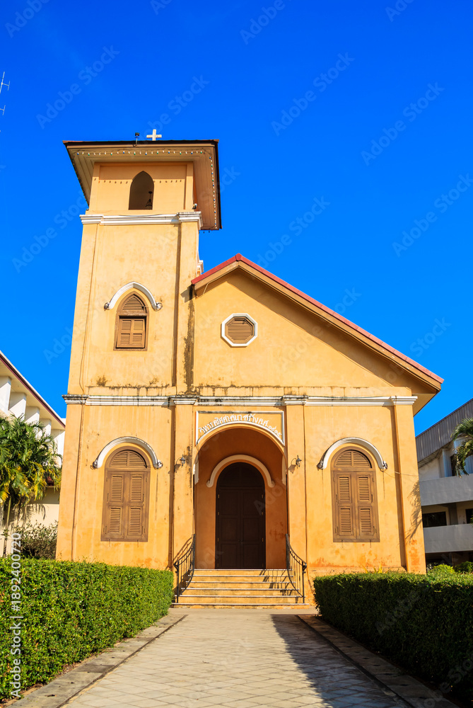 Fototapeta premium Beautiful vintage yellow Christian church architecture with cross symbol against blue sky background.