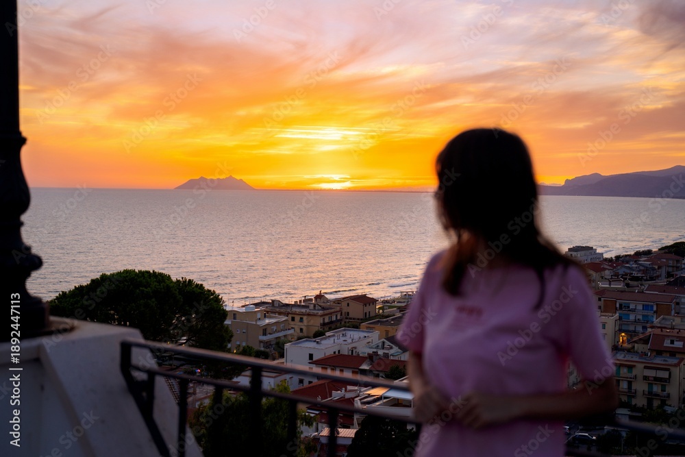 Fototapeta premium Woman watching sunset over sea from balcony