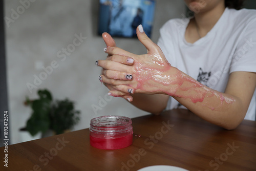 Close-up of a woman's hands in the process of skin care - a girl applies a pink scrub, gently cleansing and exfoliating the skin. The treatment symbolizes home spa care, self-care, beauty and health