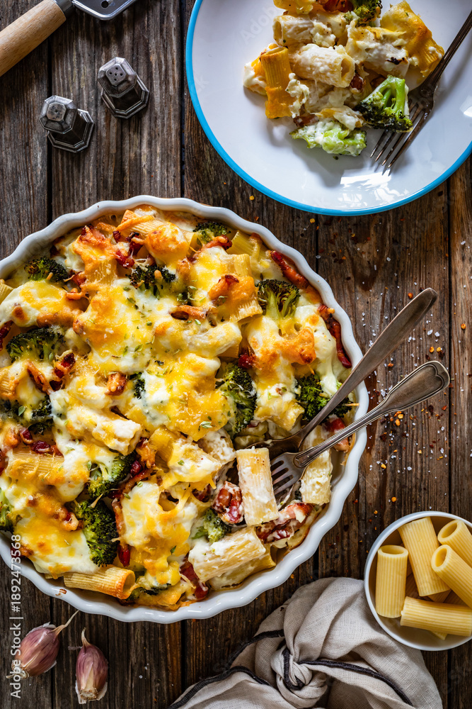 Fototapeta premium Pasta casserole with broccoli and smoked bacon on wooden table. Top view