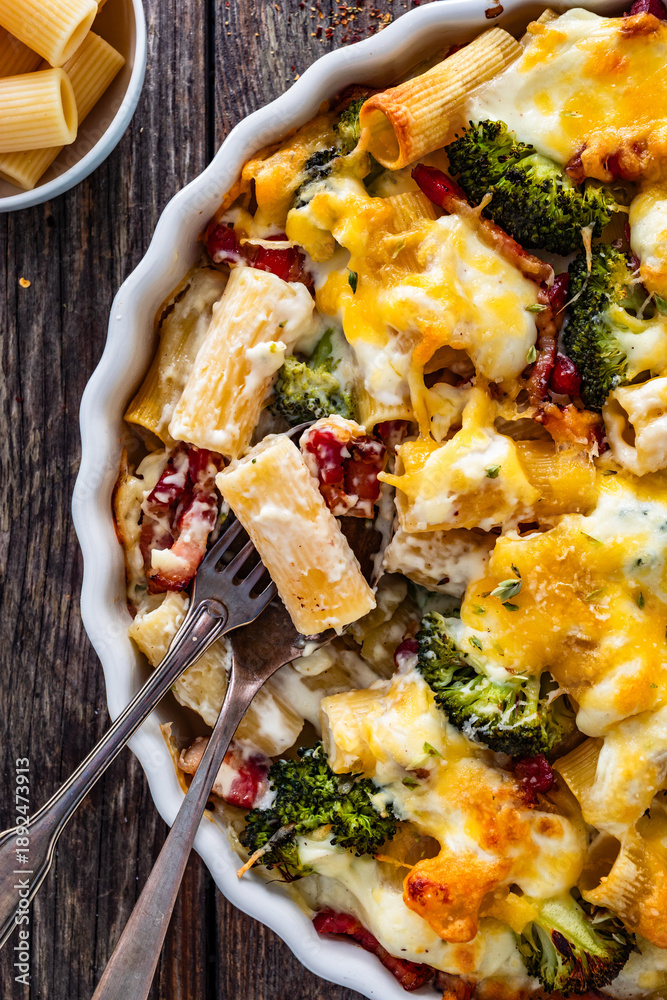 Fototapeta premium Pasta casserole with broccoli and smoked bacon on wooden table. Top view