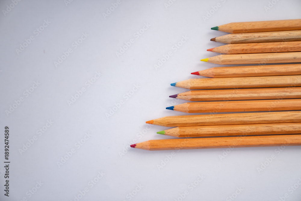Fototapeta premium Minimal flat lay composition of colorful wooden pencils on a clean white background with copy space, representing creativity, education, and art concept.