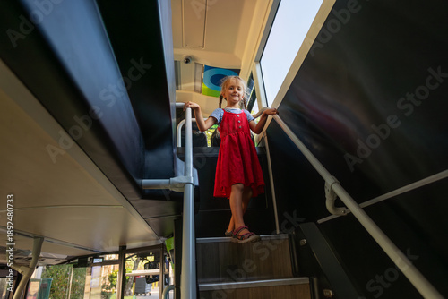 Bilde på lerret Young girl in red dress climb stairs inside a double decker bus
