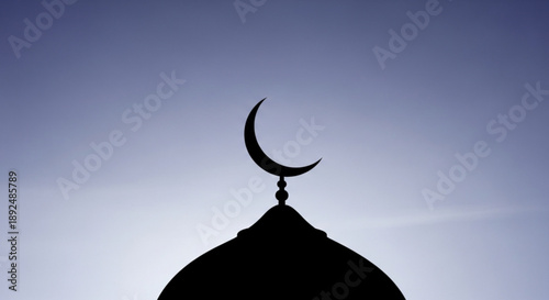 Silhouette of a mosque dome with a crescent moon finial against a gradient blue sky with clouds at sunset or sunrise