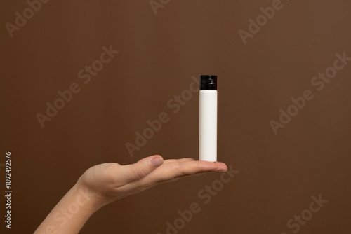 Hand holding white cosmetic bottle, brown background