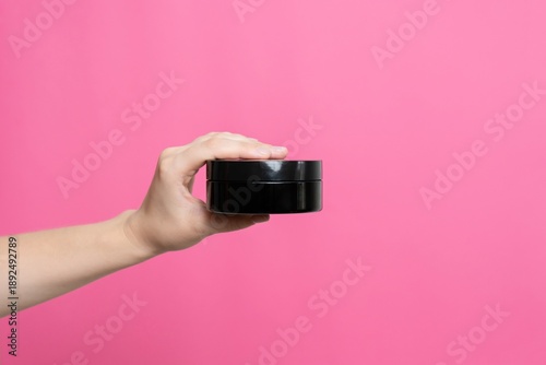 Wallpaper Mural Hand holding black cosmetic jar against pink background Torontodigital.ca