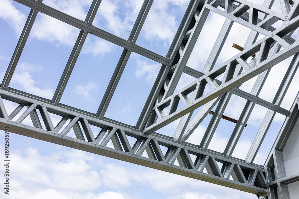 Obraz premium Close-up of a modern galvanized light steel frame LSF construction. Architectural details of roof trusses and wall framing against a blue sky. A sustainable and efficient building material.