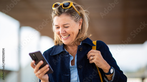 Happy senior woman looking at smartphone and laughing outdoors