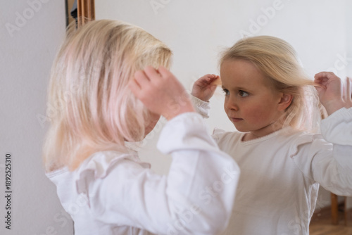 Cute little blonde girl admiring herself in the mirror.