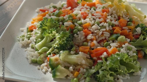 Colorful and healthy vegetable rice salad served on a white square plate, a nutritious meal.