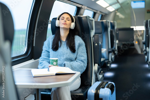A woman enjoys a peaceful moment in a train, sipping coffee while listening to music with headphones.