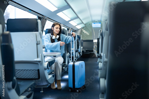 Φωτογραφία A seated woman with a suitcase in a train, showcasing a blend of comfort, style, and excitement for travel