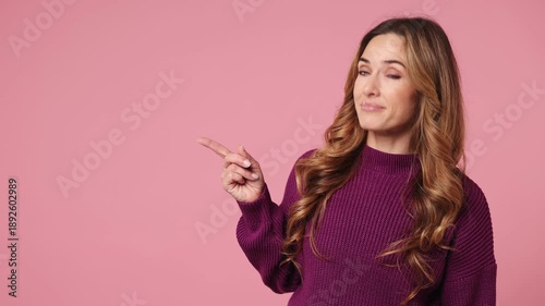Young woman wear purple knitted sweater casual clothes point indicate index finger aside on workspace area copy space mock up isolated on plain pastel light pink background studio. Lifestyle concept